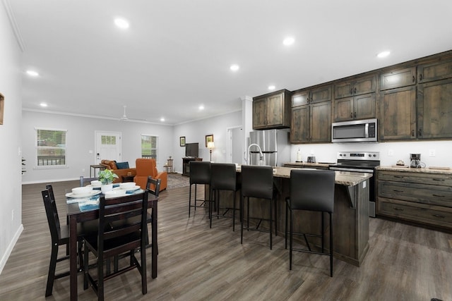 kitchen featuring appliances with stainless steel finishes, a kitchen breakfast bar, crown molding, a kitchen island with sink, and dark hardwood / wood-style floors