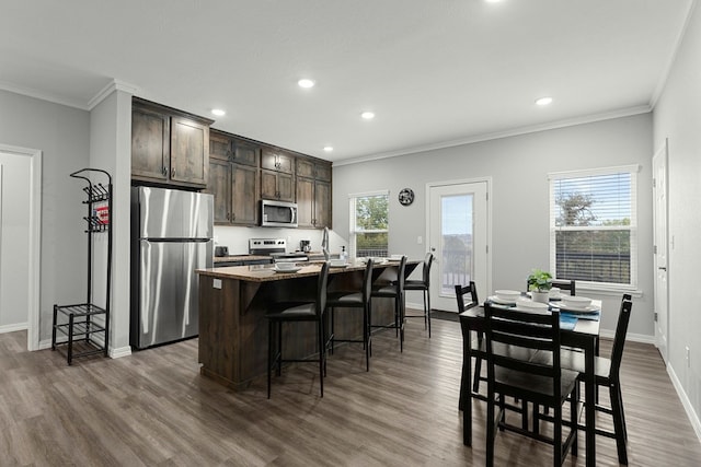 kitchen featuring a kitchen breakfast bar, an island with sink, stainless steel appliances, dark brown cabinetry, and dark hardwood / wood-style floors