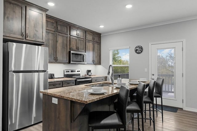 kitchen with ornamental molding, dark brown cabinetry, light wood finished floors, stainless steel appliances, and light stone counters