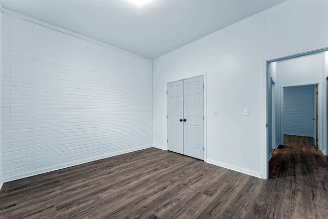 unfurnished bedroom featuring brick wall, a closet, and dark hardwood / wood-style flooring