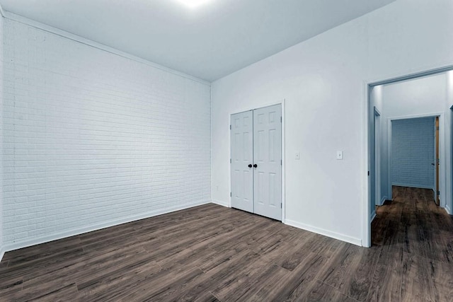 unfurnished bedroom featuring brick wall, dark wood-style flooring, a closet, and baseboards