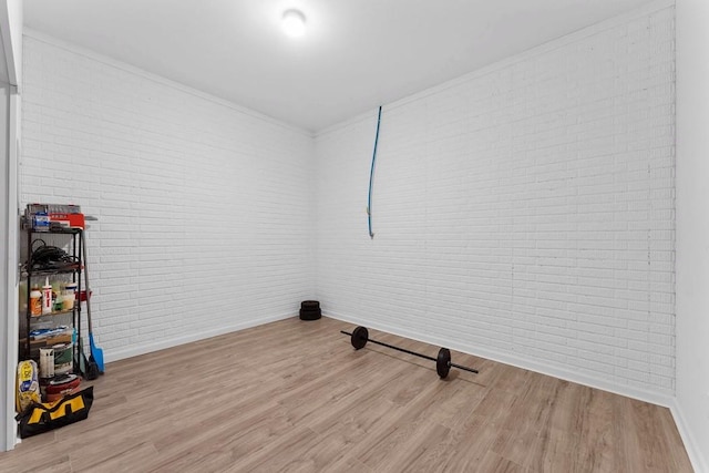 clothes washing area with brick wall, light wood-type flooring, and baseboards