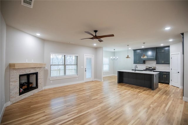 kitchen with a kitchen island with sink, ceiling fan with notable chandelier, sink, stainless steel stove, and a fireplace