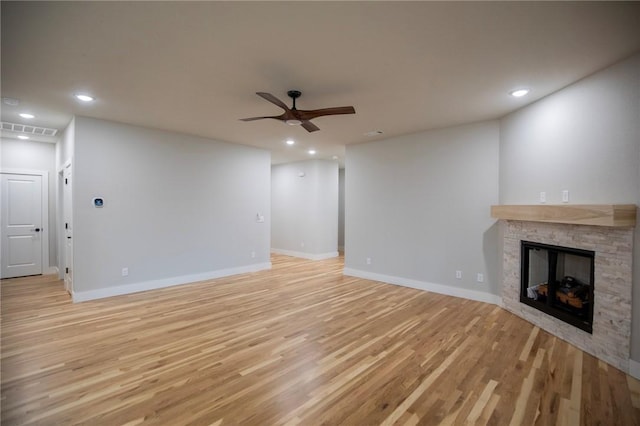 unfurnished living room with light hardwood / wood-style flooring, a stone fireplace, and ceiling fan