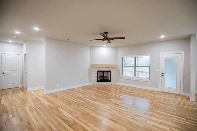 unfurnished living room with a stone fireplace, ceiling fan, and light hardwood / wood-style floors