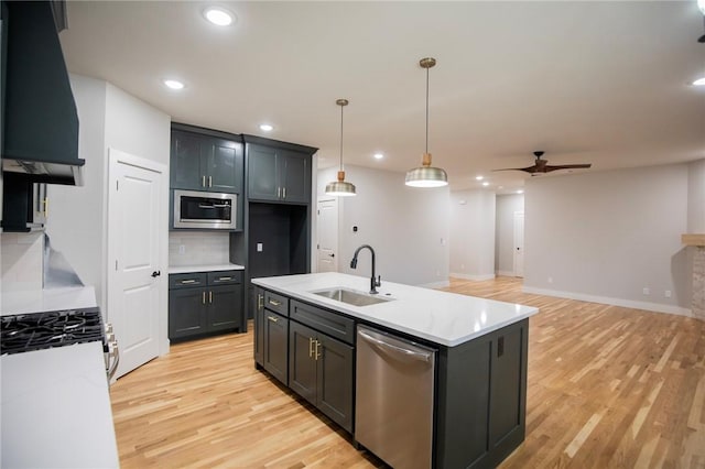 kitchen featuring a center island with sink, sink, ceiling fan, range hood, and stainless steel appliances