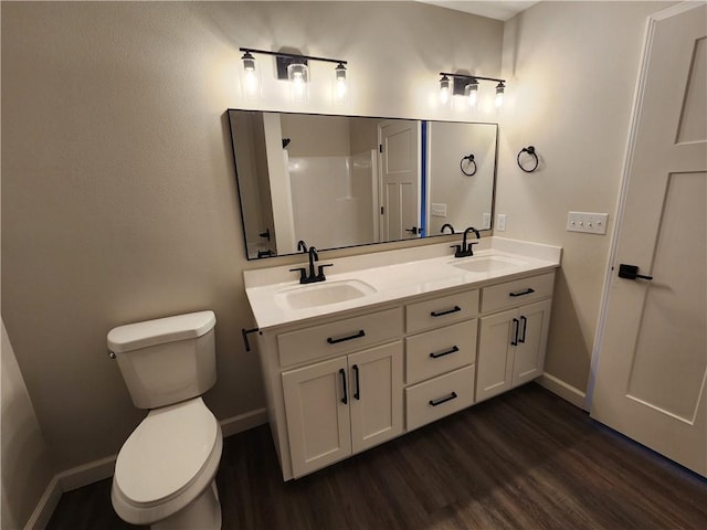 full bathroom with toilet, double vanity, a sink, and wood finished floors