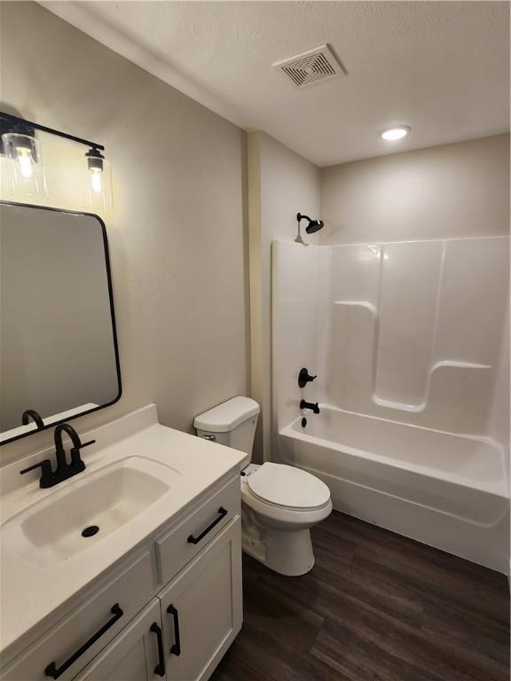 bathroom featuring visible vents, toilet, washtub / shower combination, vanity, and wood finished floors