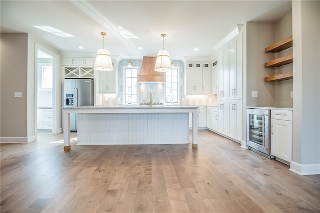 kitchen featuring an island with sink, wine cooler, light wood-type flooring, and white cabinetry