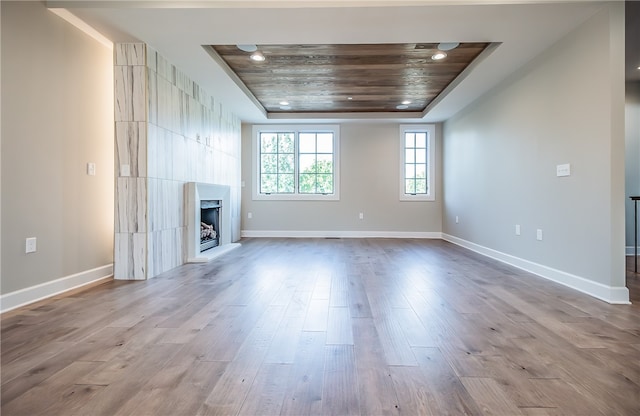 unfurnished living room featuring a raised ceiling, wood ceiling, and light hardwood / wood-style flooring