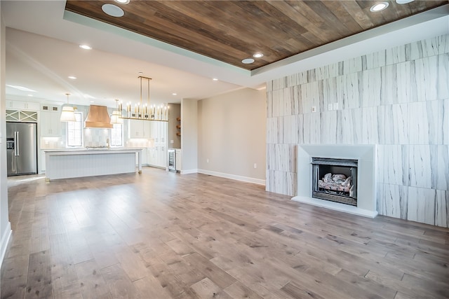 unfurnished living room featuring light hardwood / wood-style flooring, a raised ceiling, and wooden ceiling