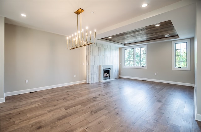 unfurnished living room with hardwood / wood-style flooring, a fireplace, a raised ceiling, and a notable chandelier