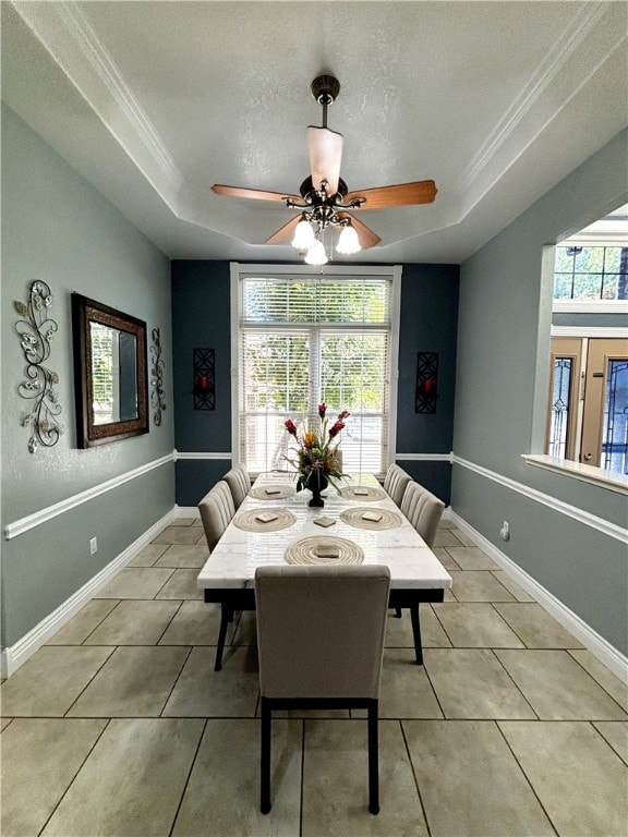 tiled dining area with ornamental molding, a tray ceiling, ceiling fan, and a healthy amount of sunlight