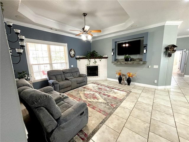 living room with ceiling fan, a raised ceiling, a tiled fireplace, and crown molding