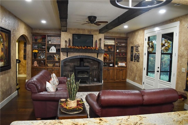 living room with built in features, dark hardwood / wood-style floors, a wood stove, and ceiling fan