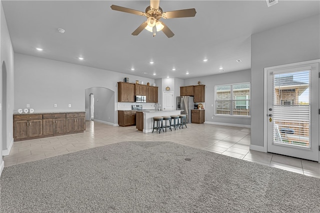 unfurnished living room with ceiling fan, sink, and light tile patterned floors