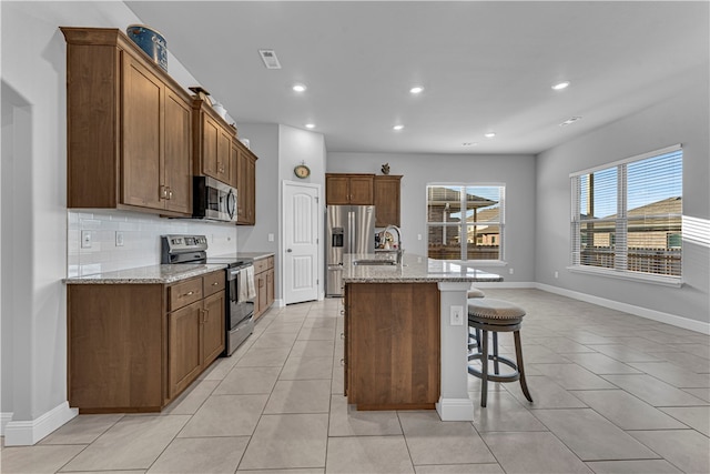 kitchen with light stone countertops, a center island with sink, appliances with stainless steel finishes, and sink