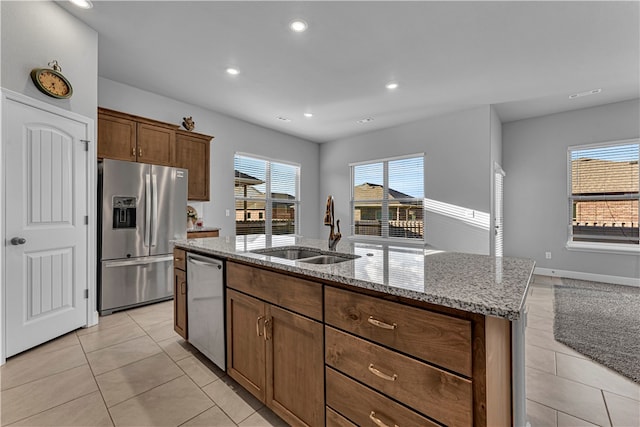 kitchen with an island with sink, light tile patterned floors, sink, appliances with stainless steel finishes, and light stone countertops