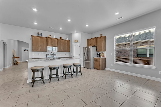 kitchen featuring a kitchen island with sink, stainless steel appliances, a kitchen breakfast bar, and light tile patterned flooring