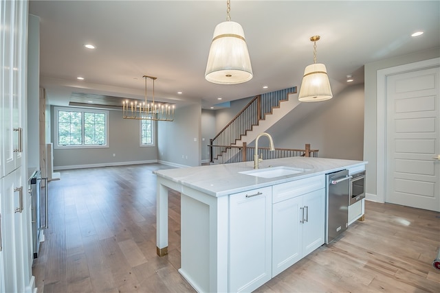 kitchen featuring hanging light fixtures, a center island with sink, white cabinetry, and sink