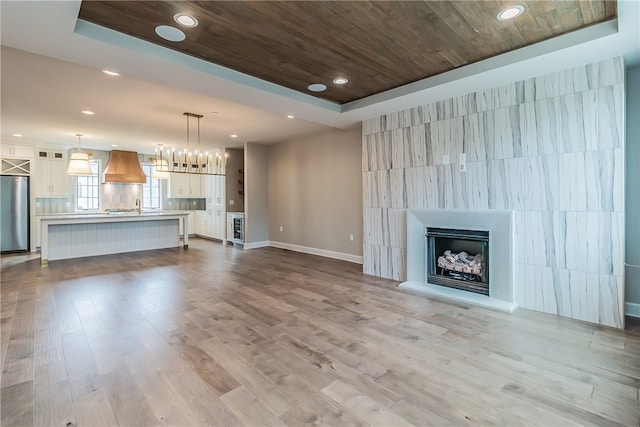 unfurnished living room with a raised ceiling, sink, wine cooler, and hardwood / wood-style flooring