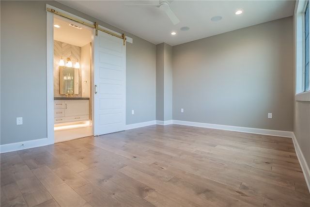 unfurnished room featuring a barn door, ceiling fan, and light hardwood / wood-style flooring