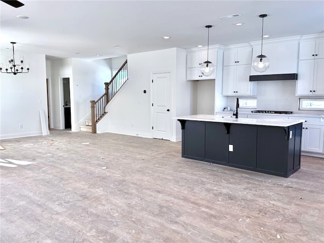 kitchen featuring an inviting chandelier, white cabinetry, hanging light fixtures, and an island with sink