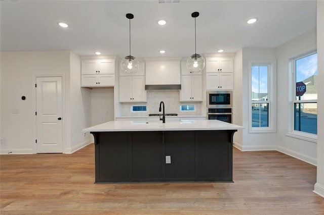 kitchen featuring built in microwave, white cabinetry, custom exhaust hood, a kitchen island with sink, and stainless steel oven