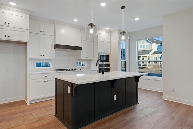 kitchen with hanging light fixtures, white cabinetry, an island with sink, and stainless steel appliances