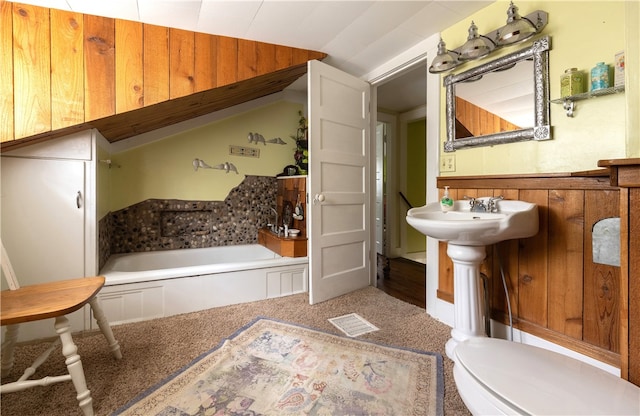 bathroom with wooden walls, lofted ceiling, a washtub, and toilet