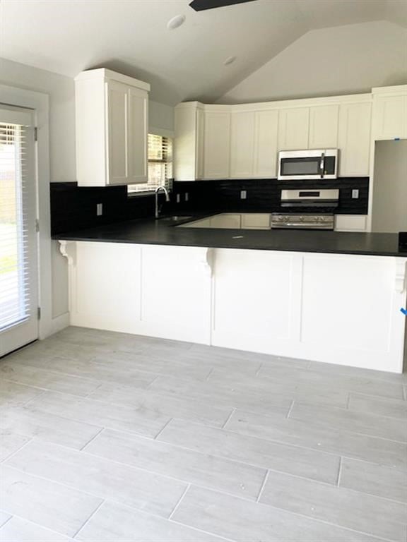 kitchen with white stove, tasteful backsplash, vaulted ceiling, and white cabinets