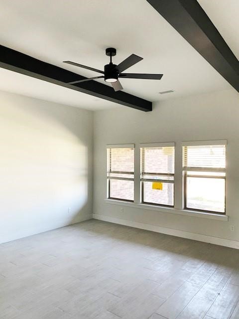 empty room with wood-type flooring, beamed ceiling, ceiling fan, and a healthy amount of sunlight