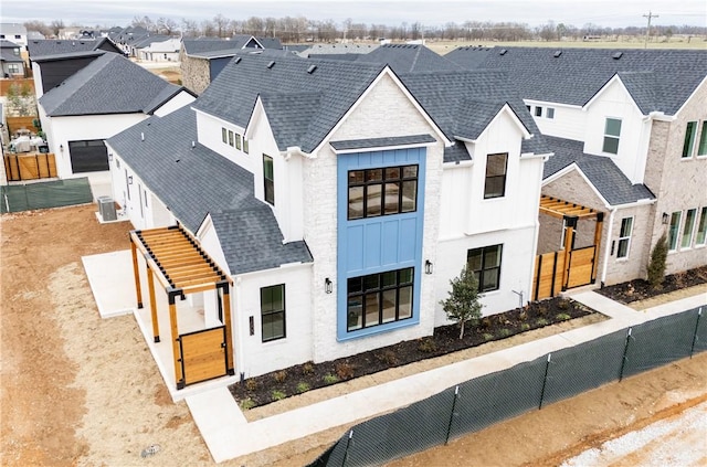 view of front of property with central AC unit, a shingled roof, board and batten siding, fence, and a residential view