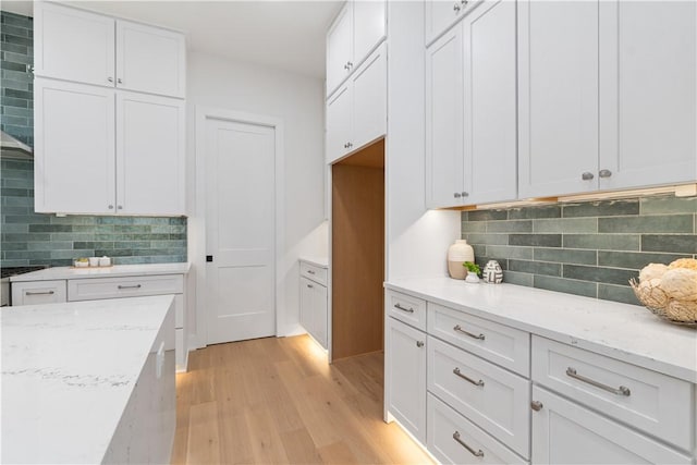 kitchen featuring white cabinets, tasteful backsplash, light wood-type flooring, and light stone countertops