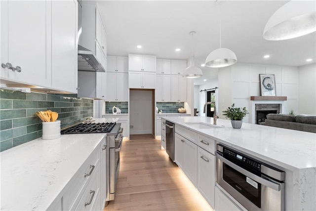 kitchen featuring a sink, decorative backsplash, white cabinetry, light wood finished floors, and appliances with stainless steel finishes