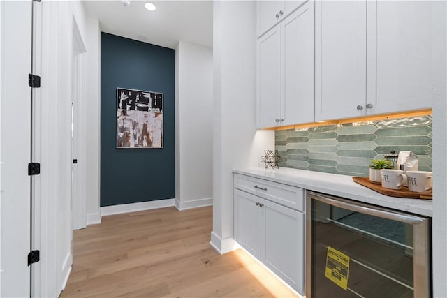 bar featuring light wood finished floors, wine cooler, a bar, baseboards, and tasteful backsplash