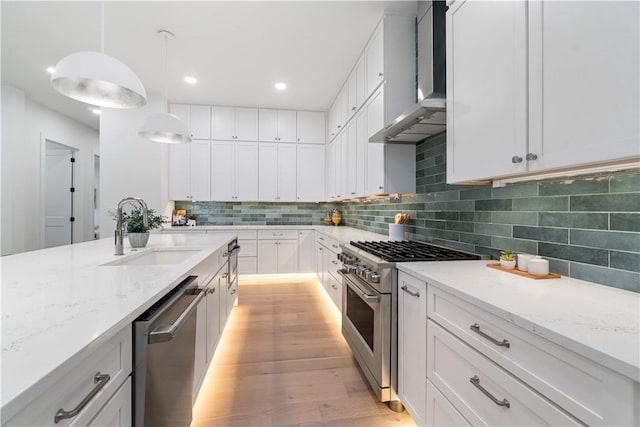 kitchen featuring stainless steel appliances, backsplash, wall chimney range hood, a sink, and light wood-style floors