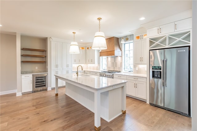 kitchen featuring white cabinets, appliances with stainless steel finishes, hanging light fixtures, and premium range hood