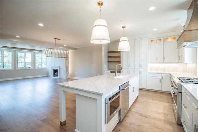 kitchen with sink, a kitchen island with sink, white cabinetry, stainless steel appliances, and custom range hood