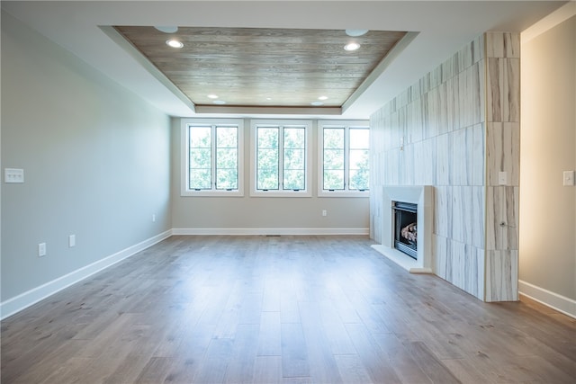 unfurnished living room featuring light wood-type flooring, a raised ceiling, and a large fireplace