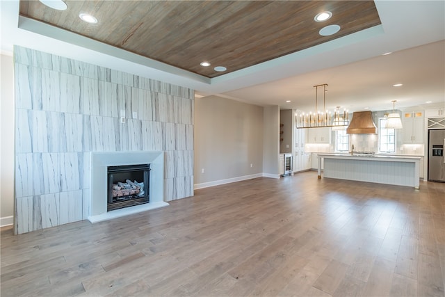 unfurnished living room with sink, a tray ceiling, light hardwood / wood-style floors, and wood ceiling