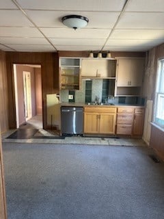 kitchen featuring dishwasher, sink, light colored carpet, a drop ceiling, and wooden walls