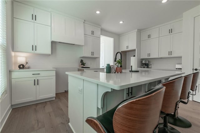 kitchen featuring light hardwood / wood-style flooring, a kitchen island with sink, tasteful backsplash, white cabinets, and a kitchen bar