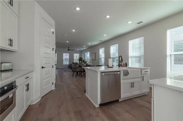 kitchen with appliances with stainless steel finishes, white cabinetry, an island with sink, sink, and light hardwood / wood-style floors