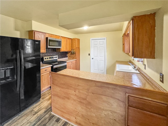 kitchen with tasteful backsplash, kitchen peninsula, stainless steel appliances, light hardwood / wood-style flooring, and sink