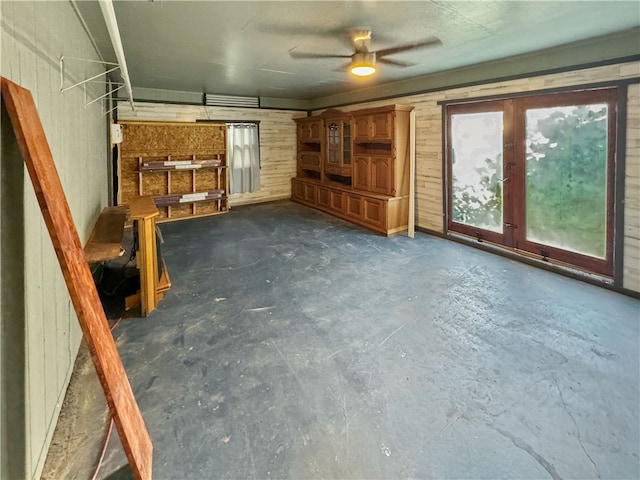 unfurnished living room featuring ceiling fan and wood walls