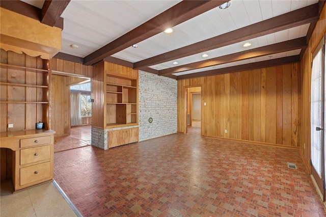 unfurnished living room featuring built in shelves, beam ceiling, and wood walls