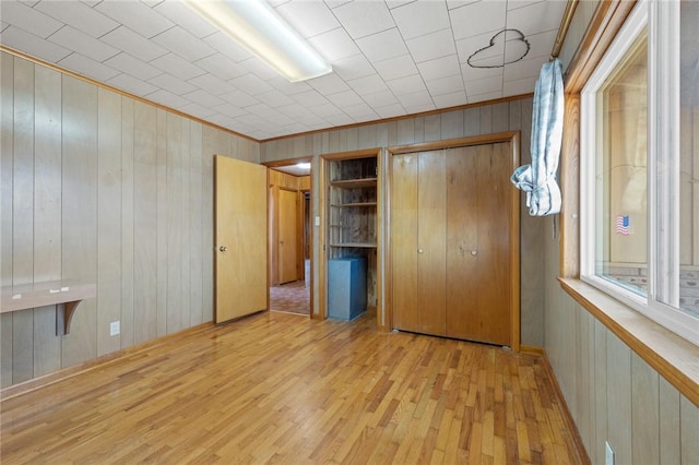 unfurnished bedroom featuring wood walls, light hardwood / wood-style floors, and a closet