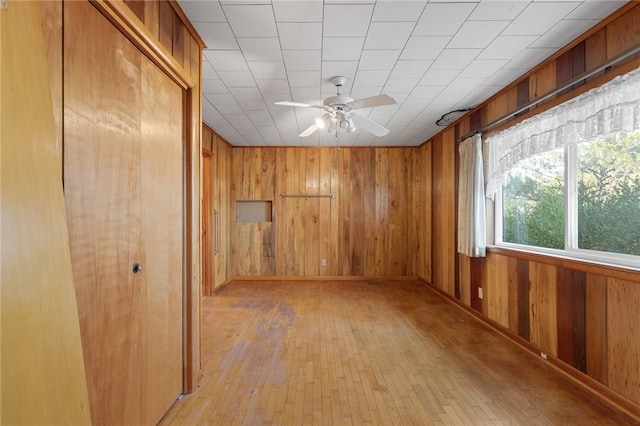 empty room with ceiling fan, light wood-type flooring, and wooden walls