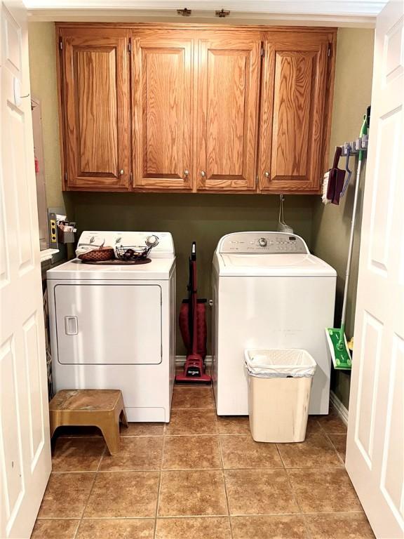 clothes washing area with cabinets, light tile patterned floors, and washing machine and clothes dryer